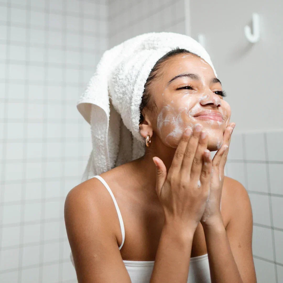 Woman washing face with cleanser in bathroom to combat hard water effects on skin