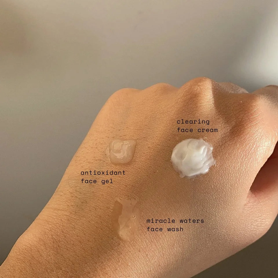 Hand with three different skincare products labeled 'antioxidant face gel', 'clearing face cream', and 'miracle waters face wash' - Ready Steady Clear Kit